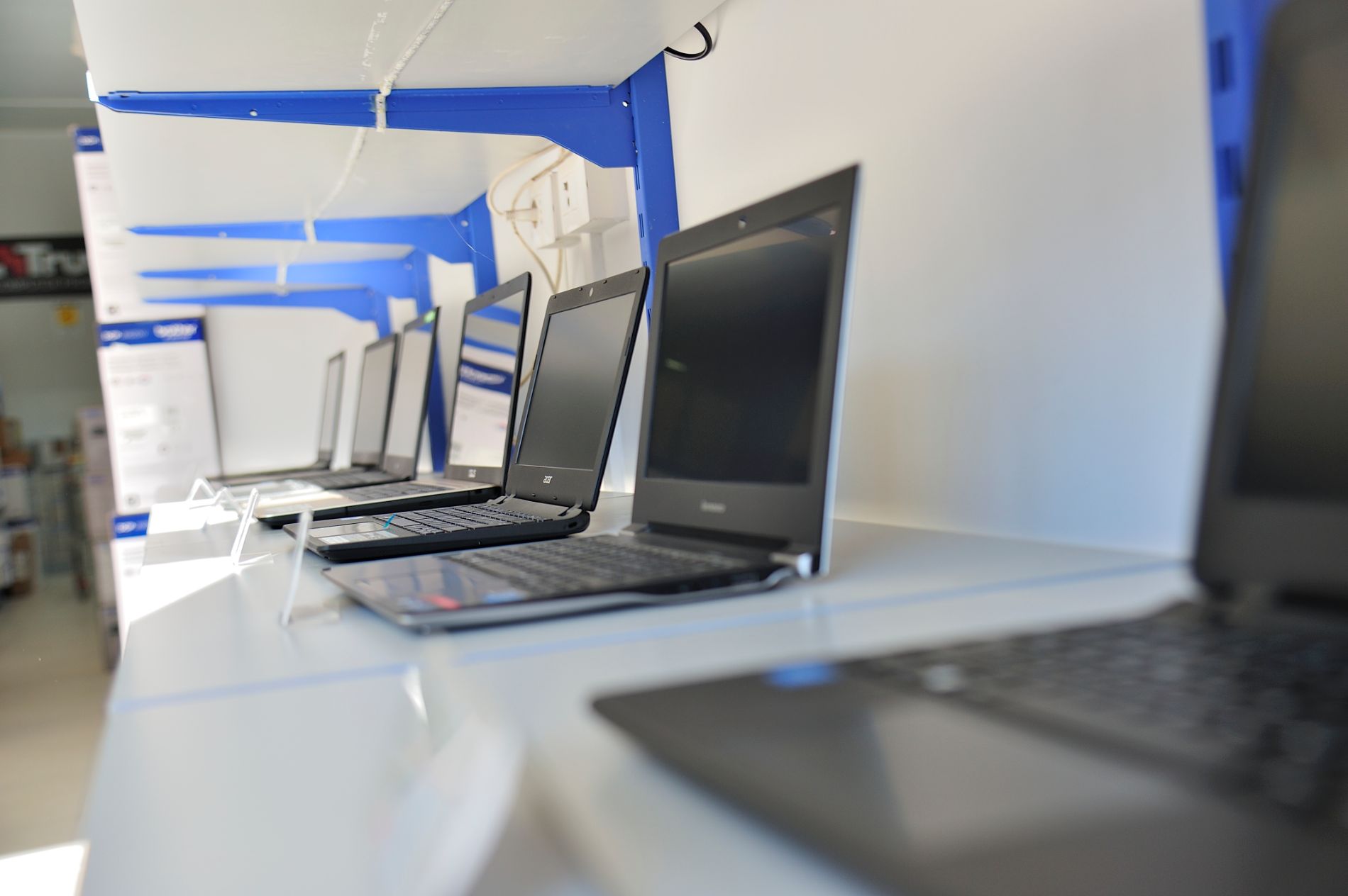 Fila di computer portatili neri su uno scaffale bianco, alcuni aperti, in un negozio con dettagli blu.