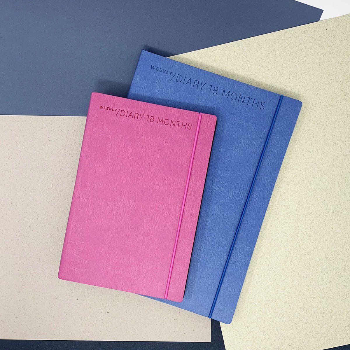 Quaderni rosa e blu con elastici su uno sfondo di carta di vari colori.