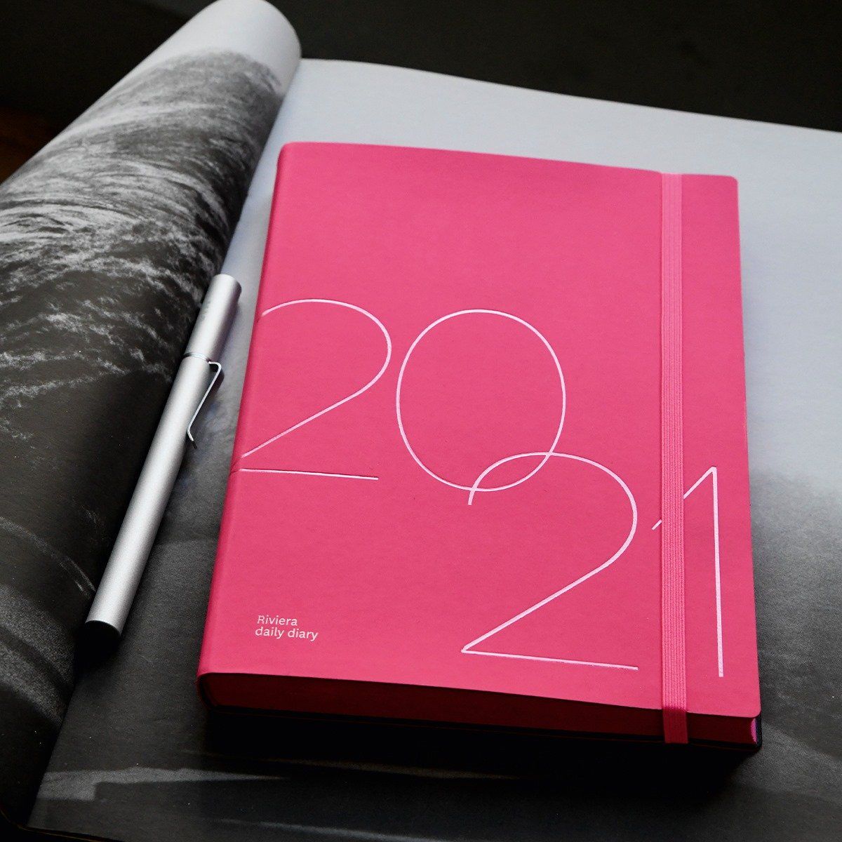 Agenda rosa 2021 con penna argentata su foto aperta in bianco e nero.