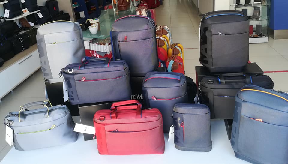 Assortimento di borse grigie, rosse e nere, alcune con cerniere rosse, esposte in un negozio.