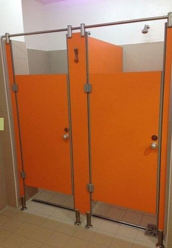 Bagni pubblici arancioni con sanitari argentati e pavimento grigio.