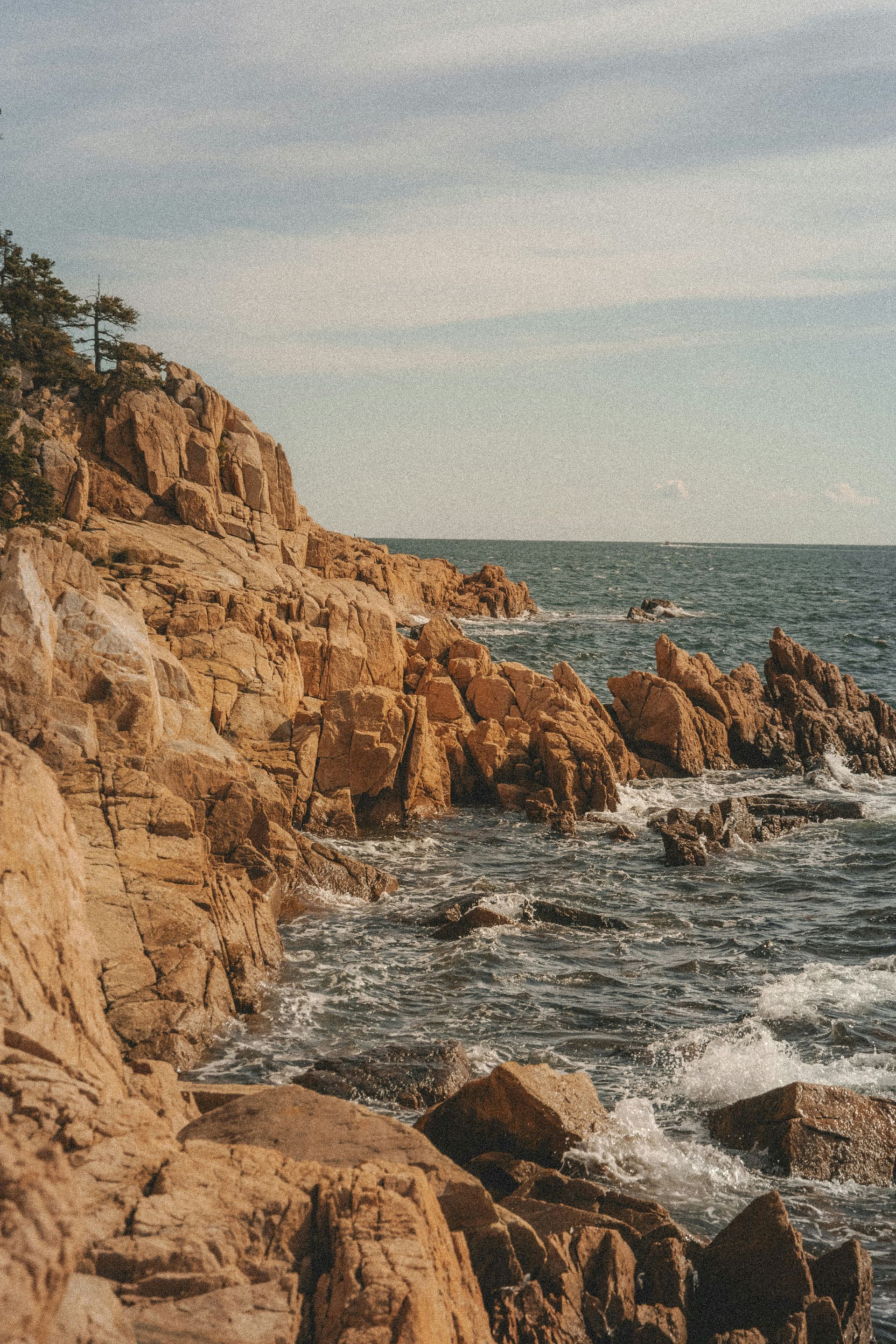 Rocky coastline with waves crashing, clear sky overhead.