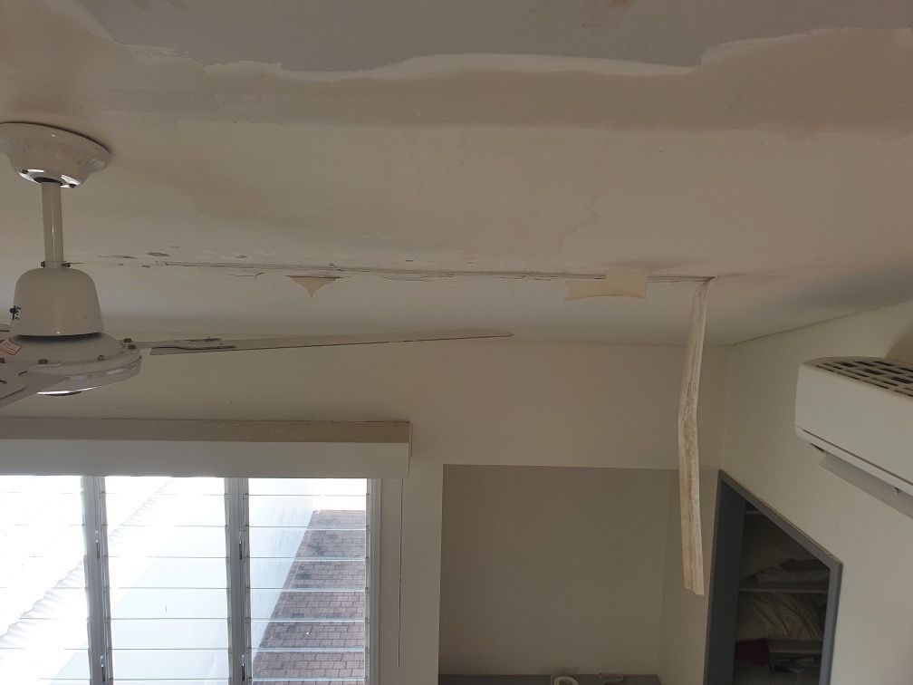 Water damage on a white ceiling, with peeling paint. A ceiling fan and window are visible — Patch Plaster Paint in Johnston, NT