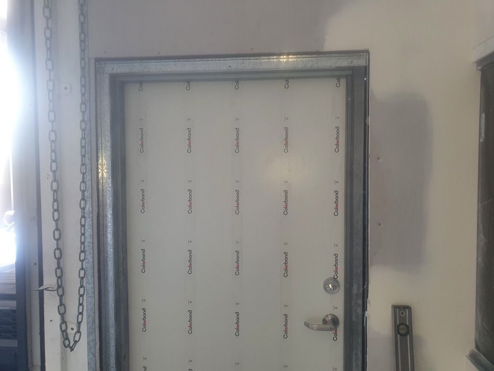 Metal door with clear plastic covering, silver frame, and handle on a white wall — Patch Plaster Paint in Johnston, NT