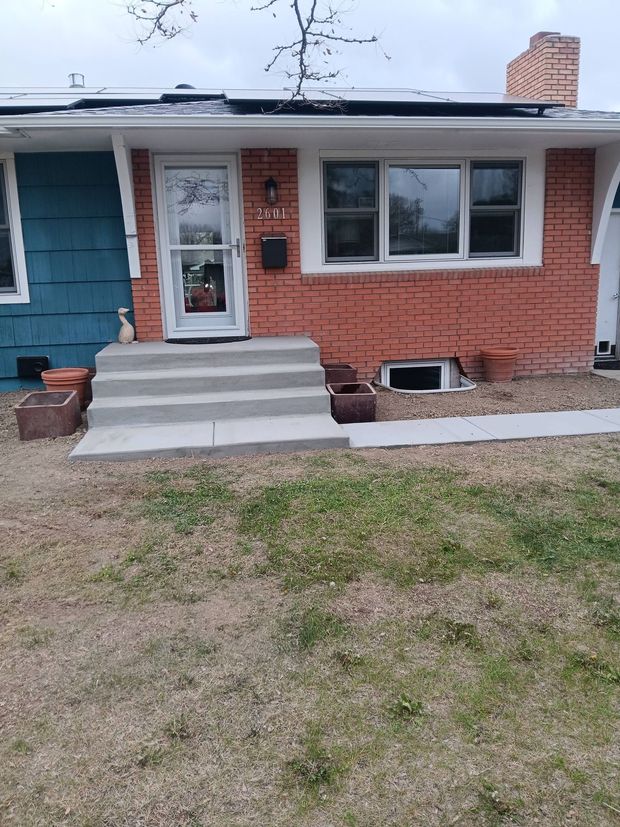 Single-story brick house with concrete steps, teal door, and a front window.