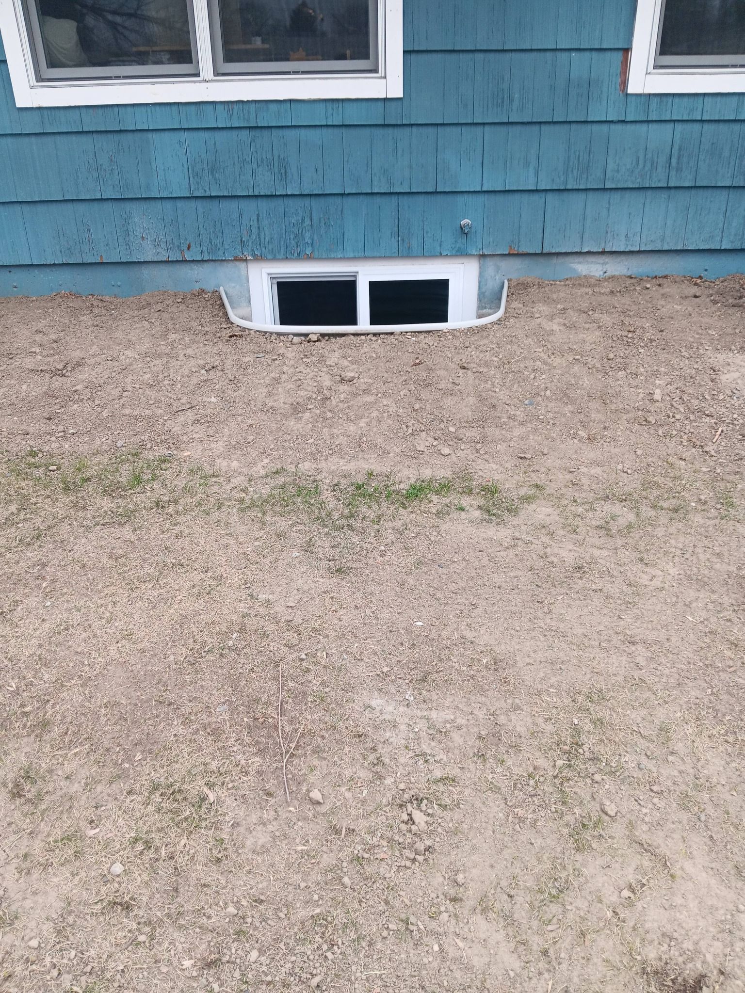 Blue house exterior with a basement window and gravel yard in front