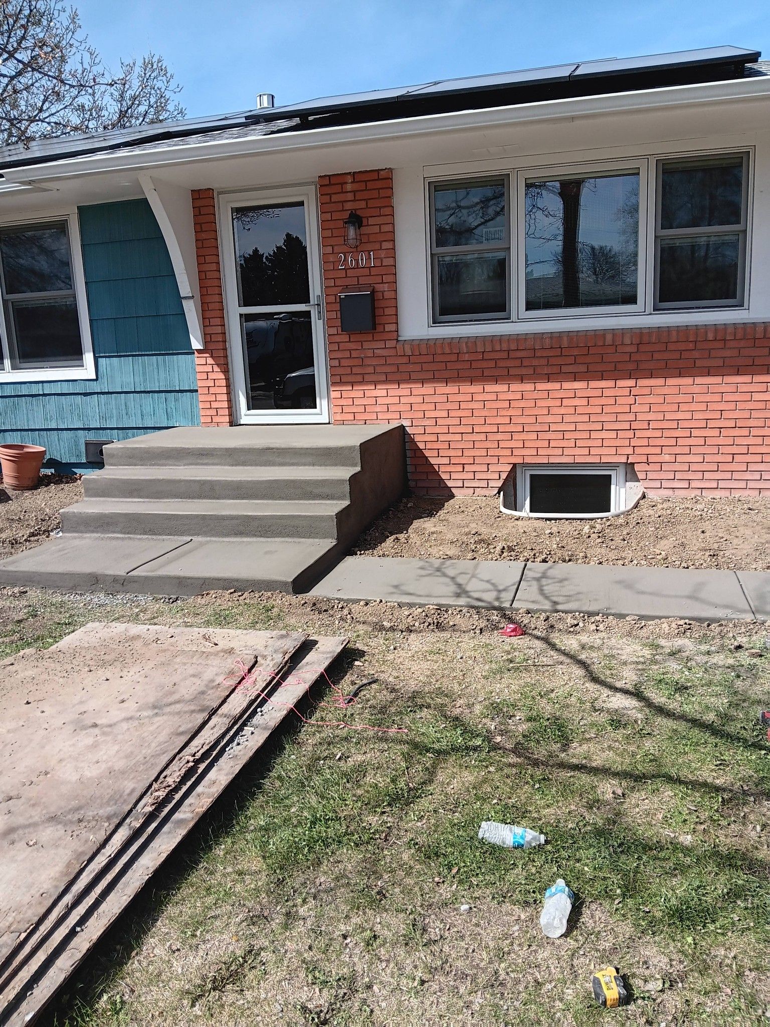 Front entrance of a house with steps, brick and blue siding, and a low basement window.