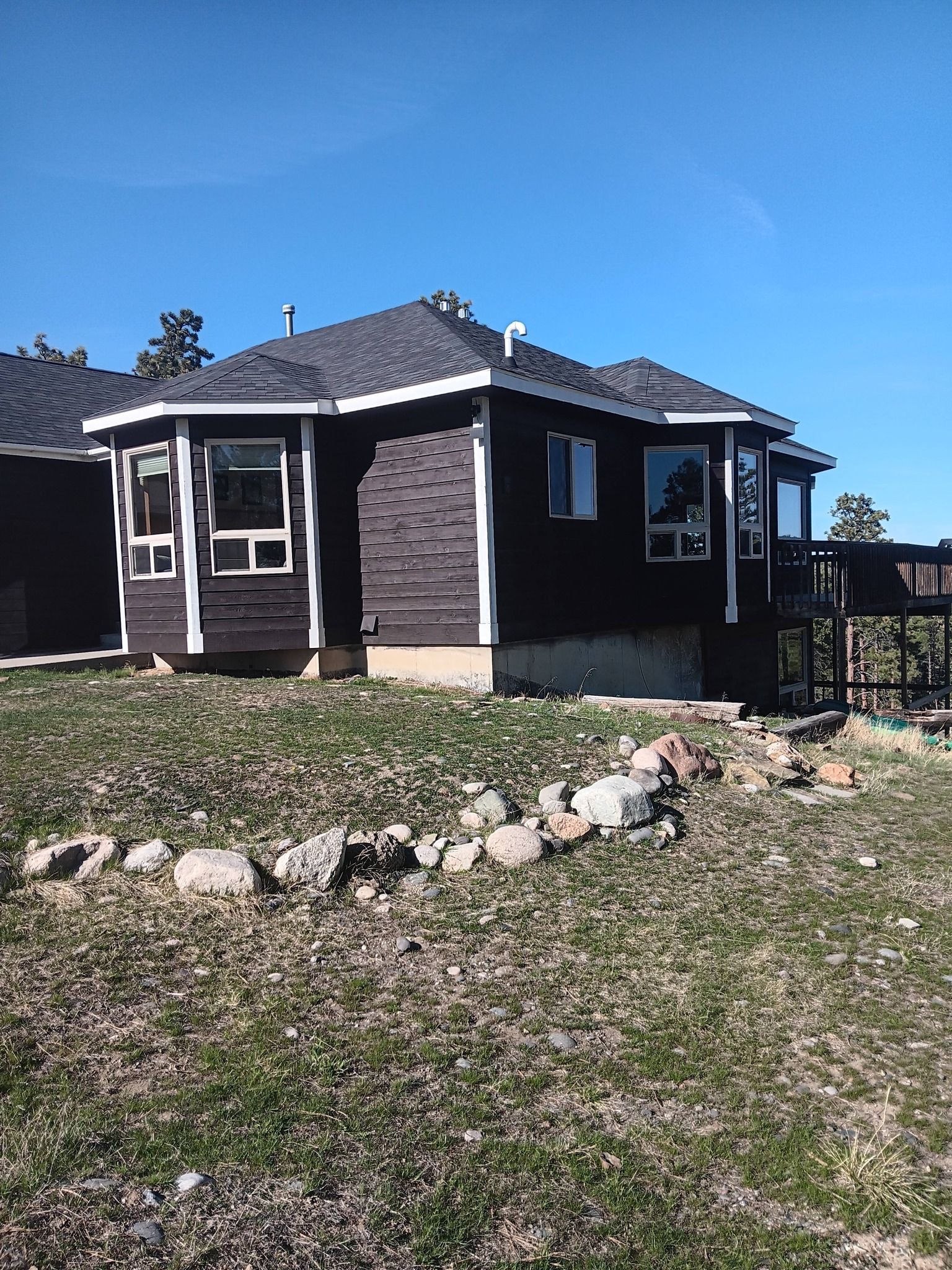 Small dark house with screened porch, rock edging, and a fenced backyard under a blue sky