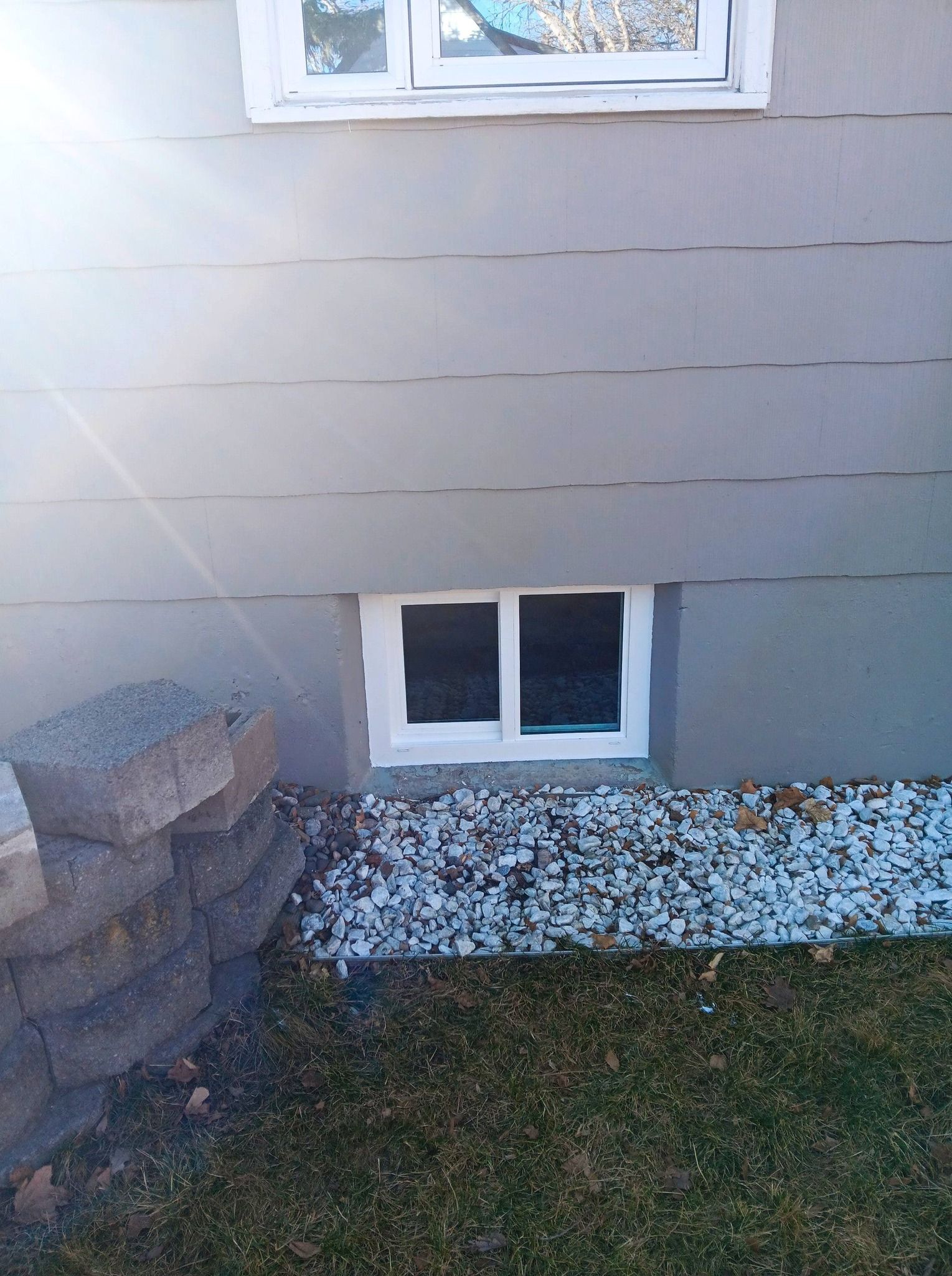 Basement window in beige house wall above stone border and grass