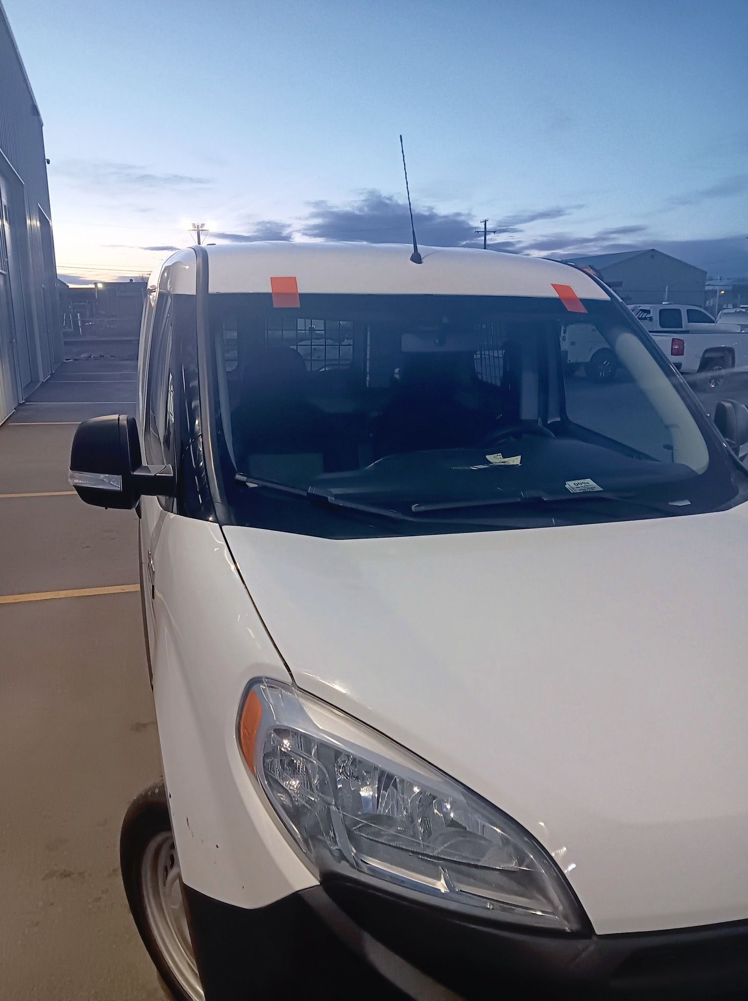 White van parked outdoors at dusk, front view with windshield and side mirror visible.