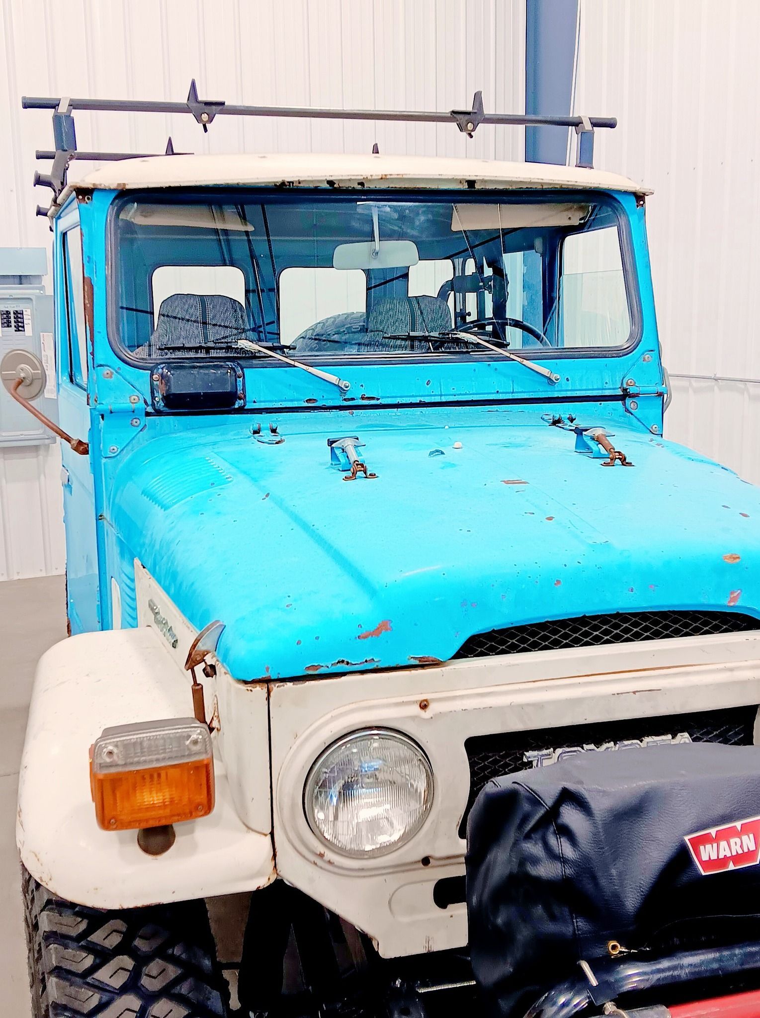 Blue vintage off-road vehicle parked by a building, front view with white bumper and round headlights