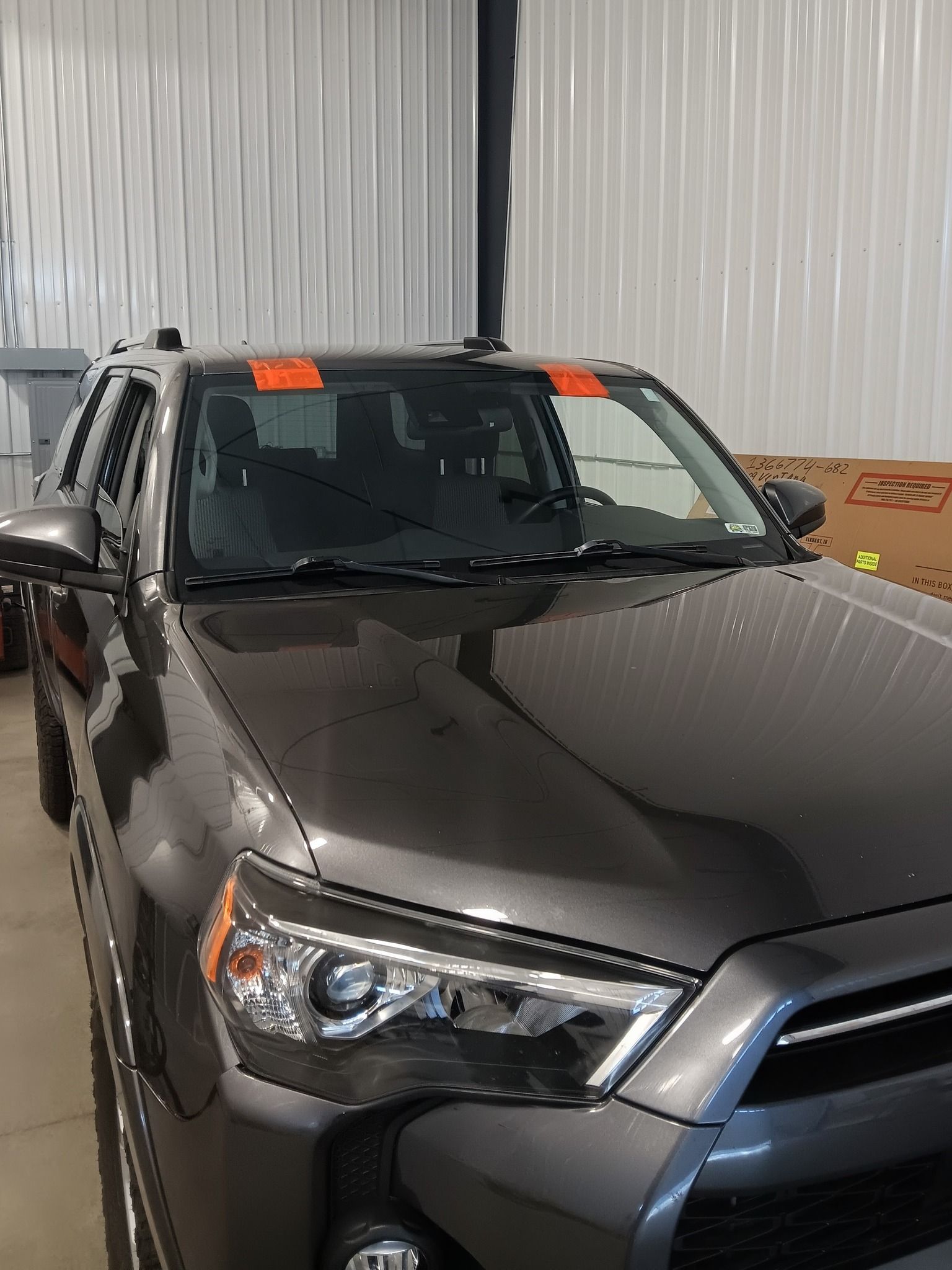 Gray SUV parked indoors near a metal wall, front-left view with orange sale tag on the windshield
