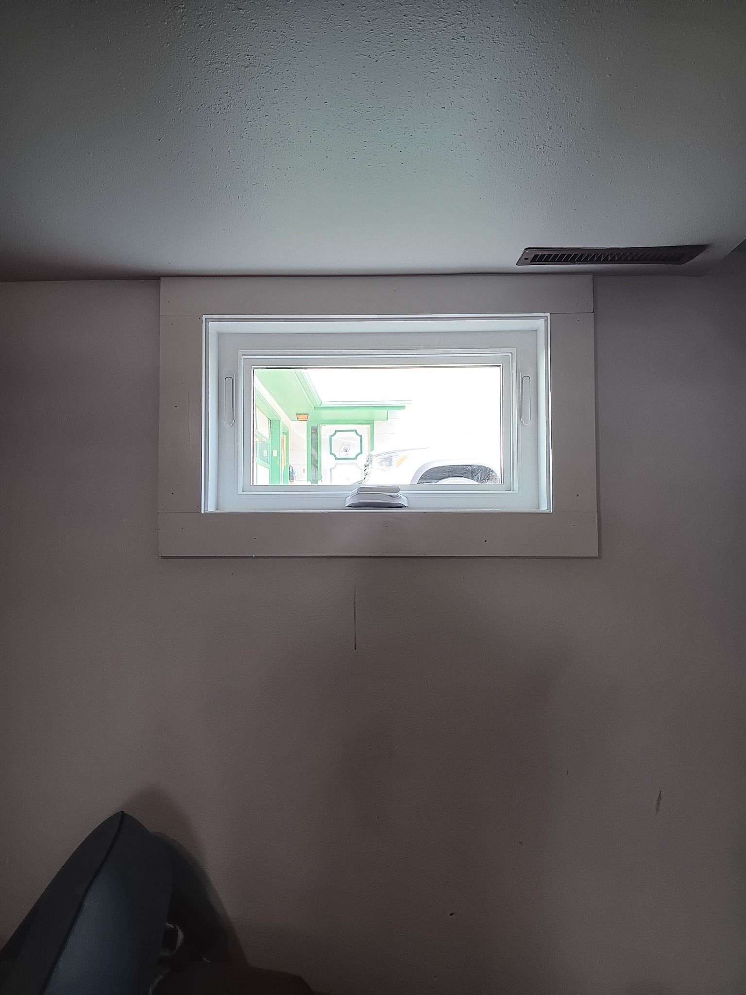 Small rectangular window in a plain room, showing greenery outside and a glimpse of a vehicle.