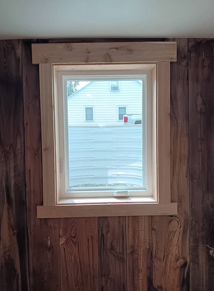 Small window with light wood trim set in dark wood-paneled wall, showing a white house outside.
