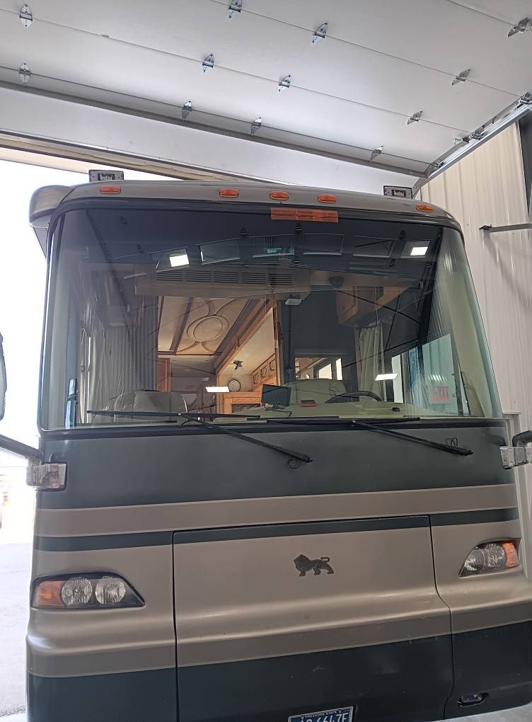 Grey bus parked inside a garage, facing forward with windshield and headlights visible