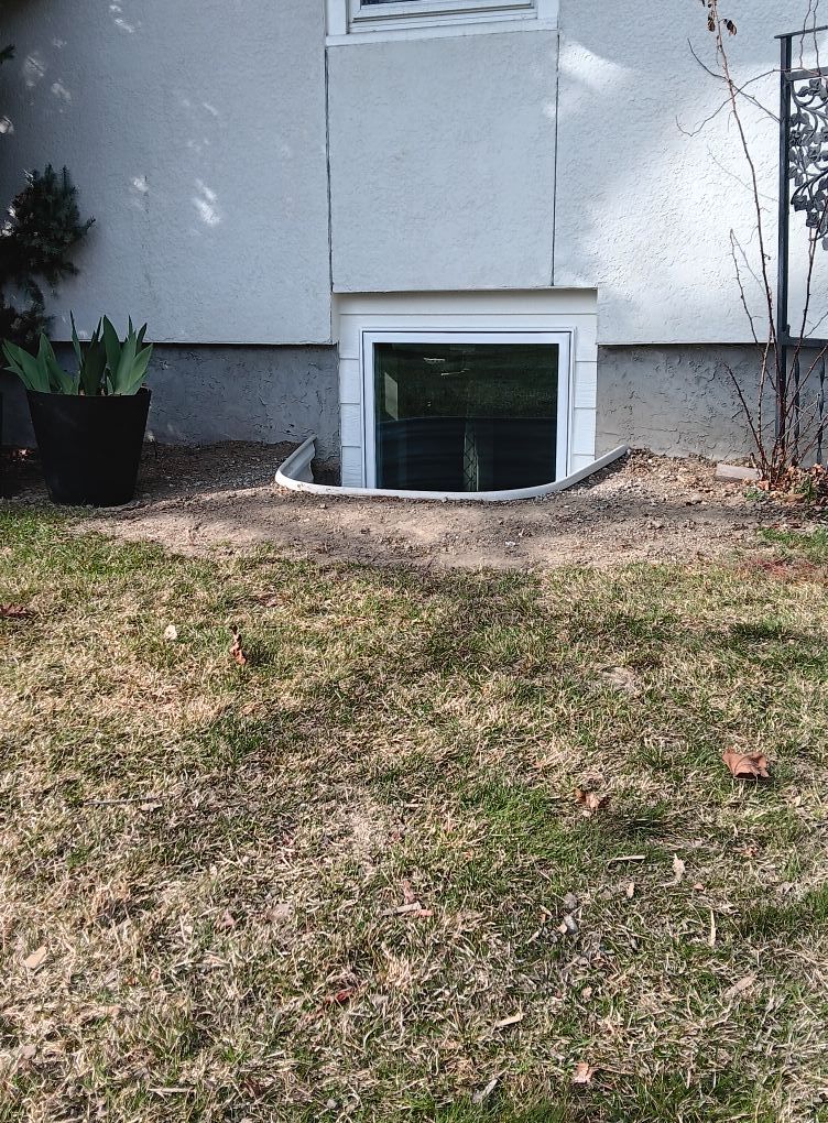 House exterior with basement window well and sloped grass lawn in front