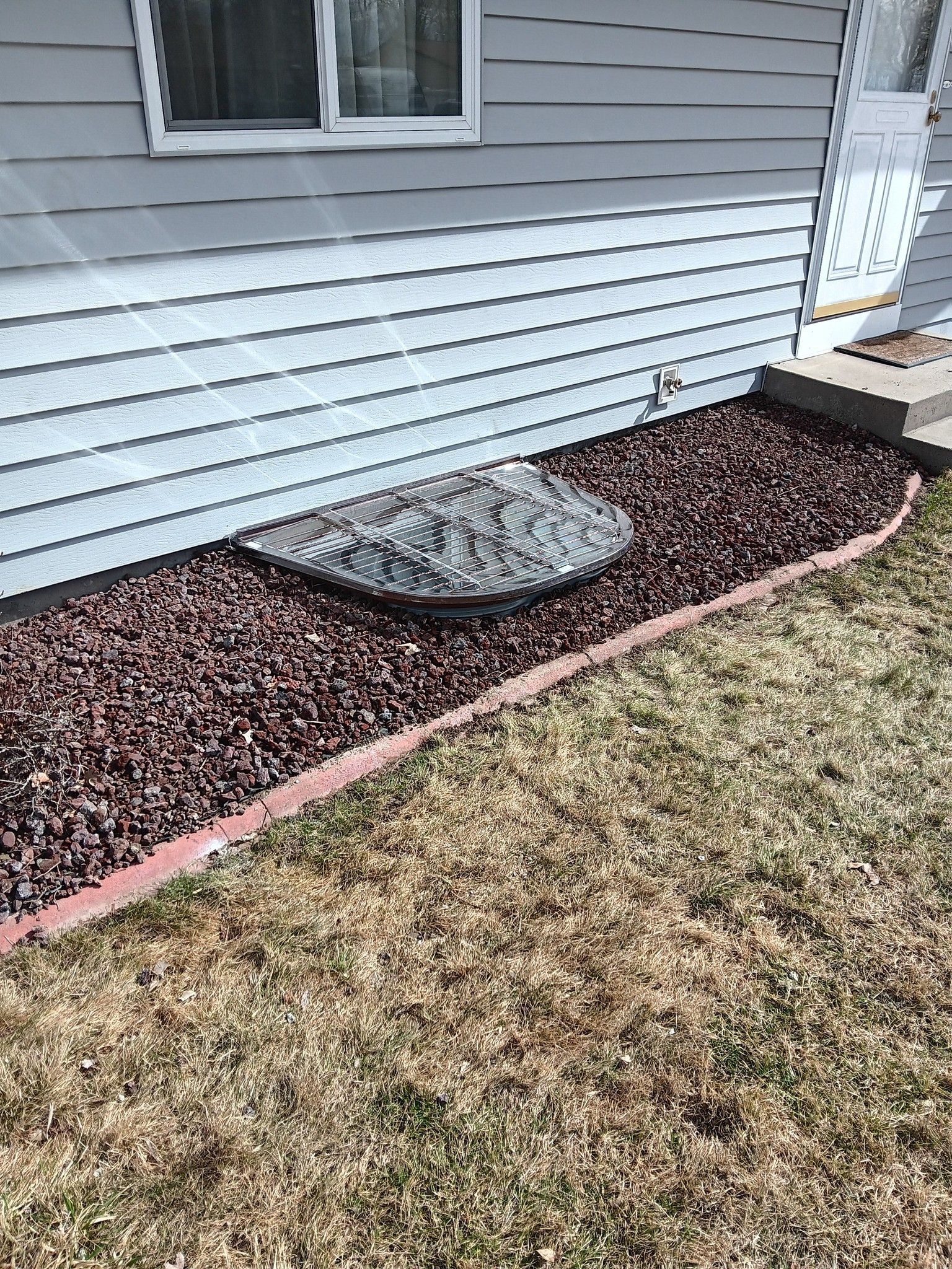 Landscape bed along house foundation with gray rocks, brown mulch, and pink edging beside siding