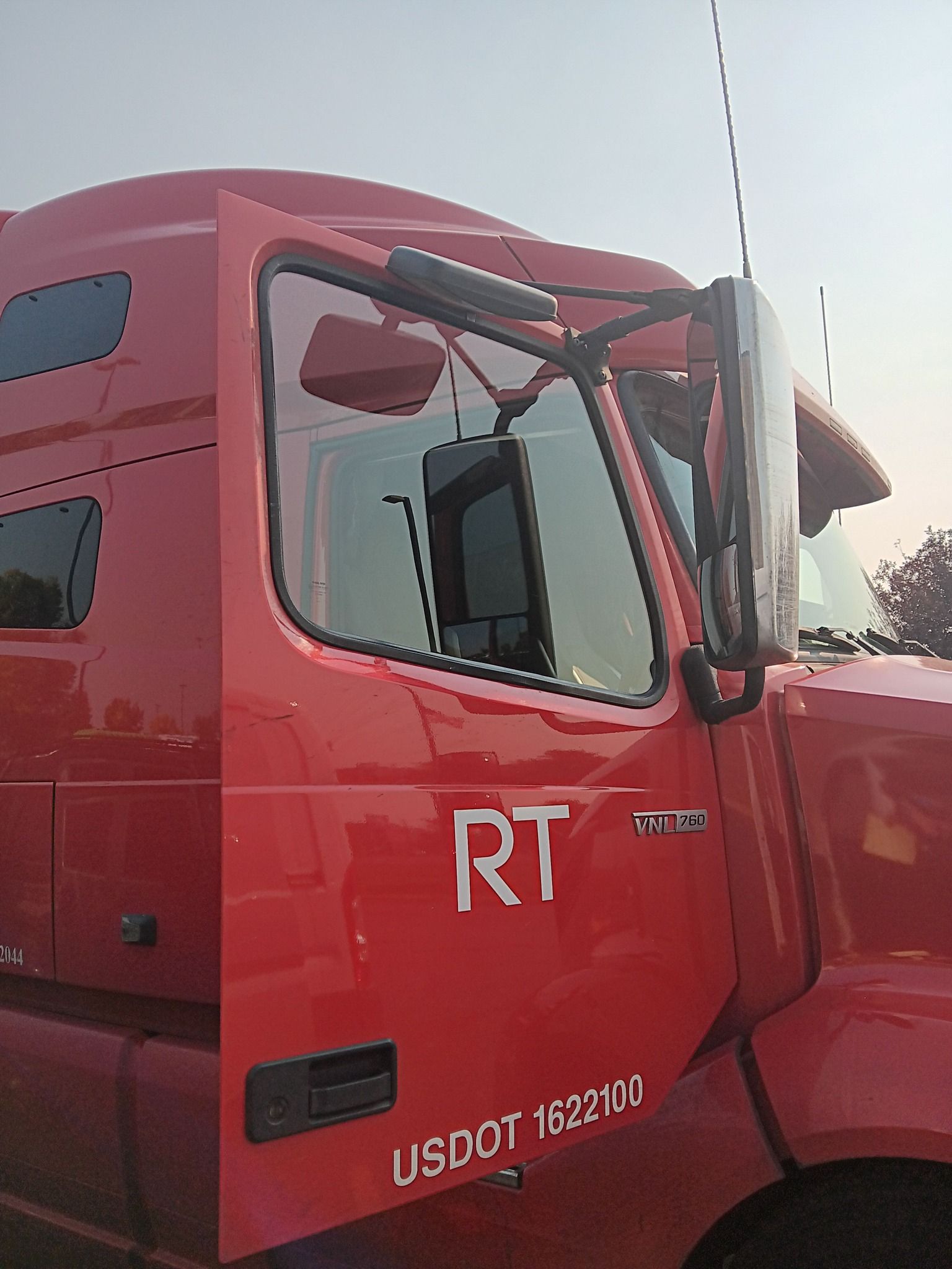 Red semi-truck cab with open door and visible side mirror, parked outdoors at dusk.