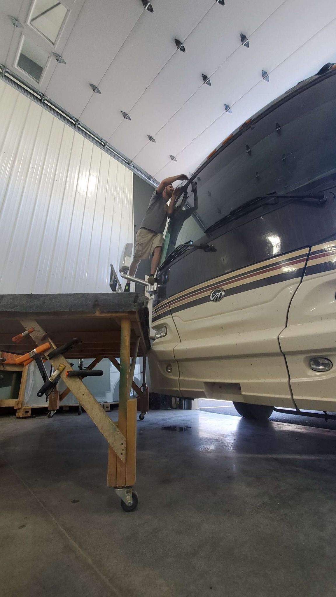 RV in a garage with a person using a ladder to work on the front windshield area