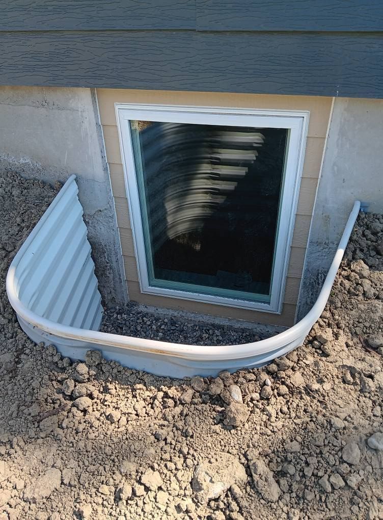 Basement window with metal well beside a house foundation and dirt soil