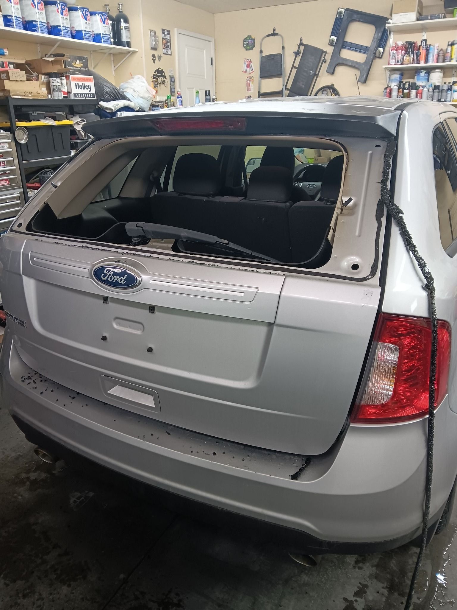 Silver Ford SUV with shattered rear window in a garage, rear view, showing visible damage