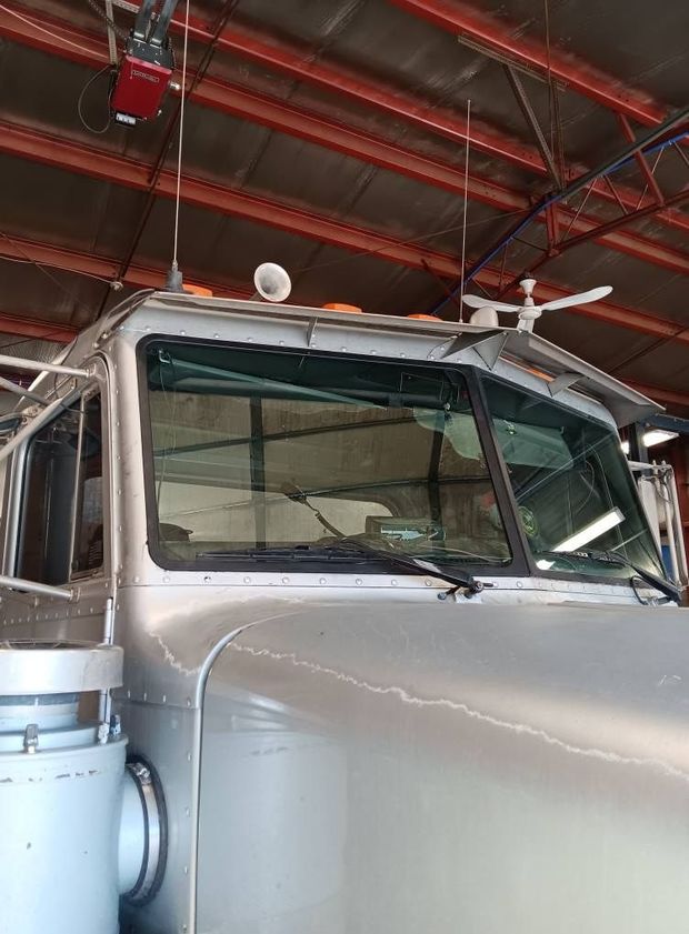 Silver truck cab inside a garage with red metal roof beams and a white ceiling fan above