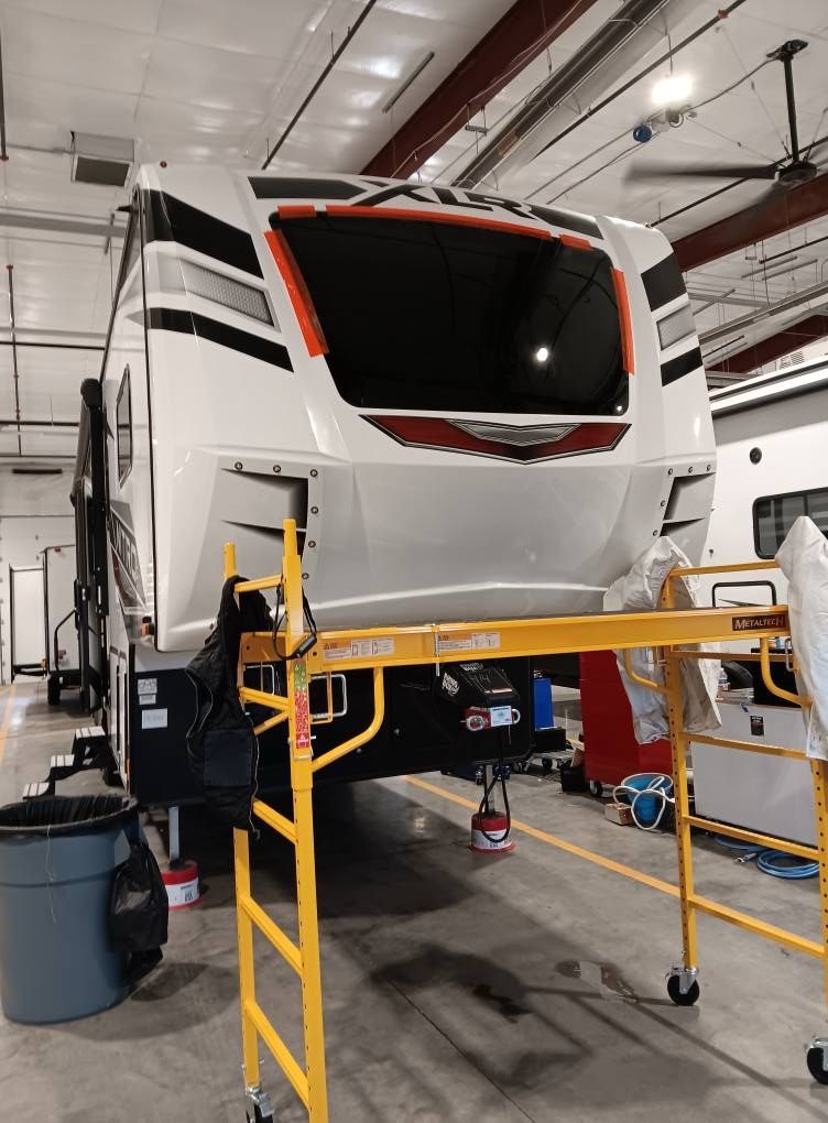 Large white RV in a garage, front elevated on jacks with yellow safety rails around it.