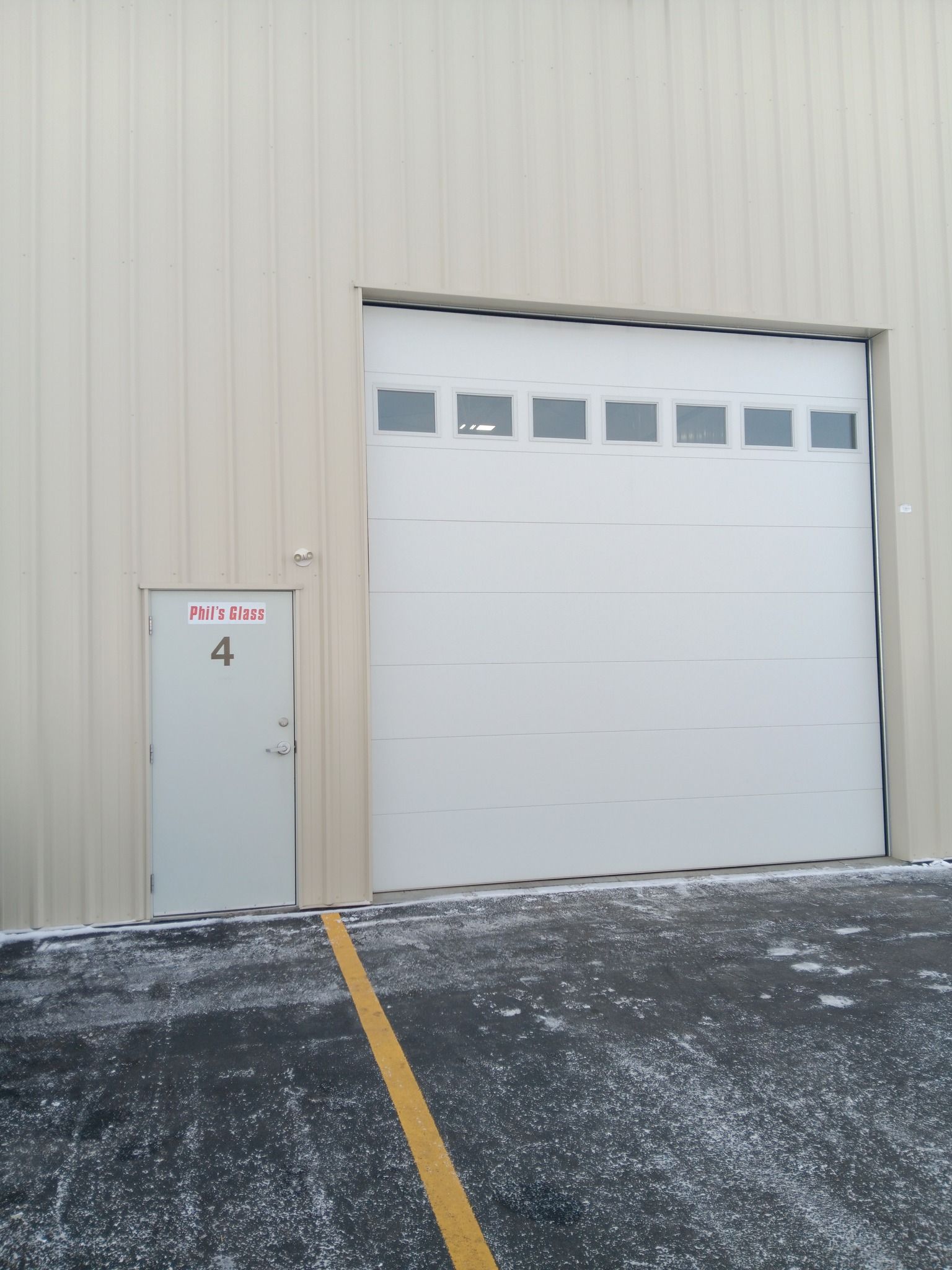 Industrial building exterior with beige metal siding, a white garage door, and snowy ground.