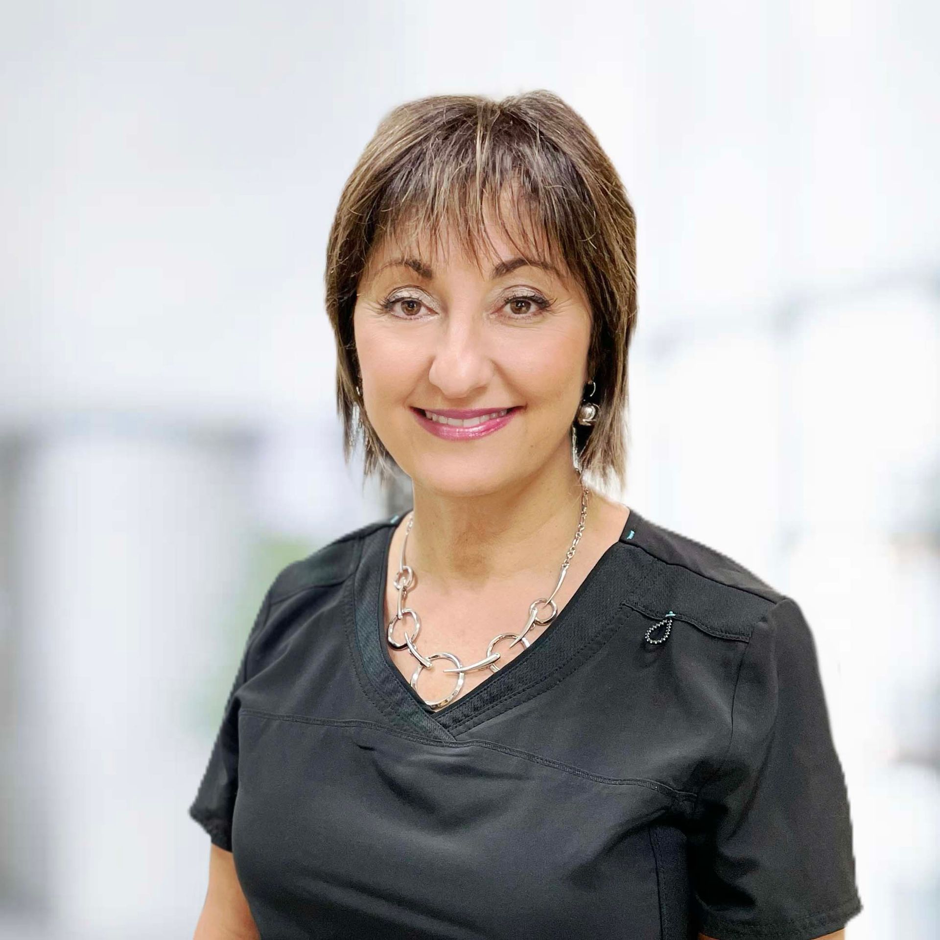 A woman wearing a black shirt and a necklace is smiling for the camera.