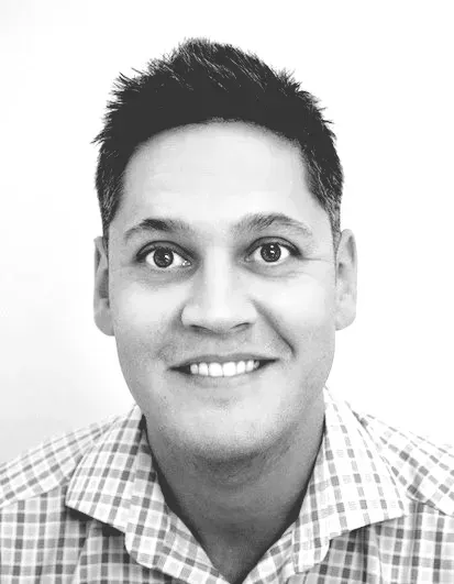 A man in a plaid shirt is smiling in a black and white photo.