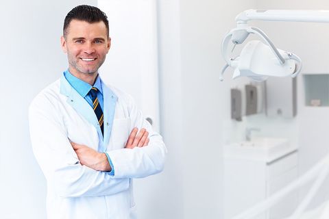 A dentist is standing in a dental office with his arms crossed.