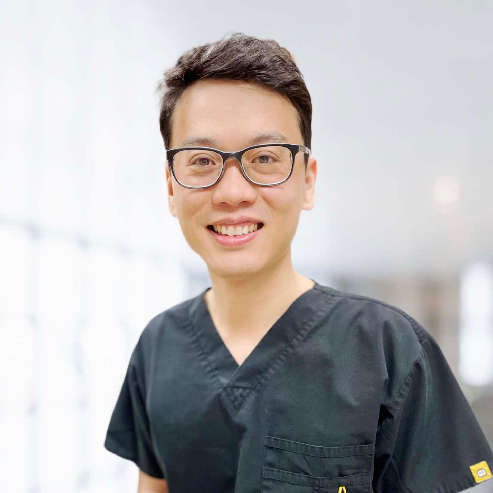 A man wearing glasses and a black scrub top is smiling for the camera.