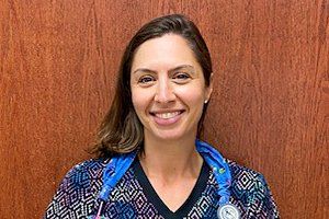 A woman in a scrub top with a stethoscope around her neck is smiling for the camera.