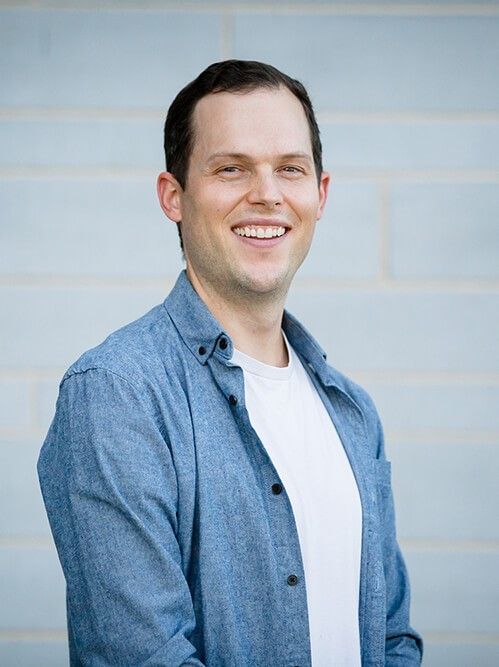 A man in a blue shirt and white shirt is smiling for the camera.