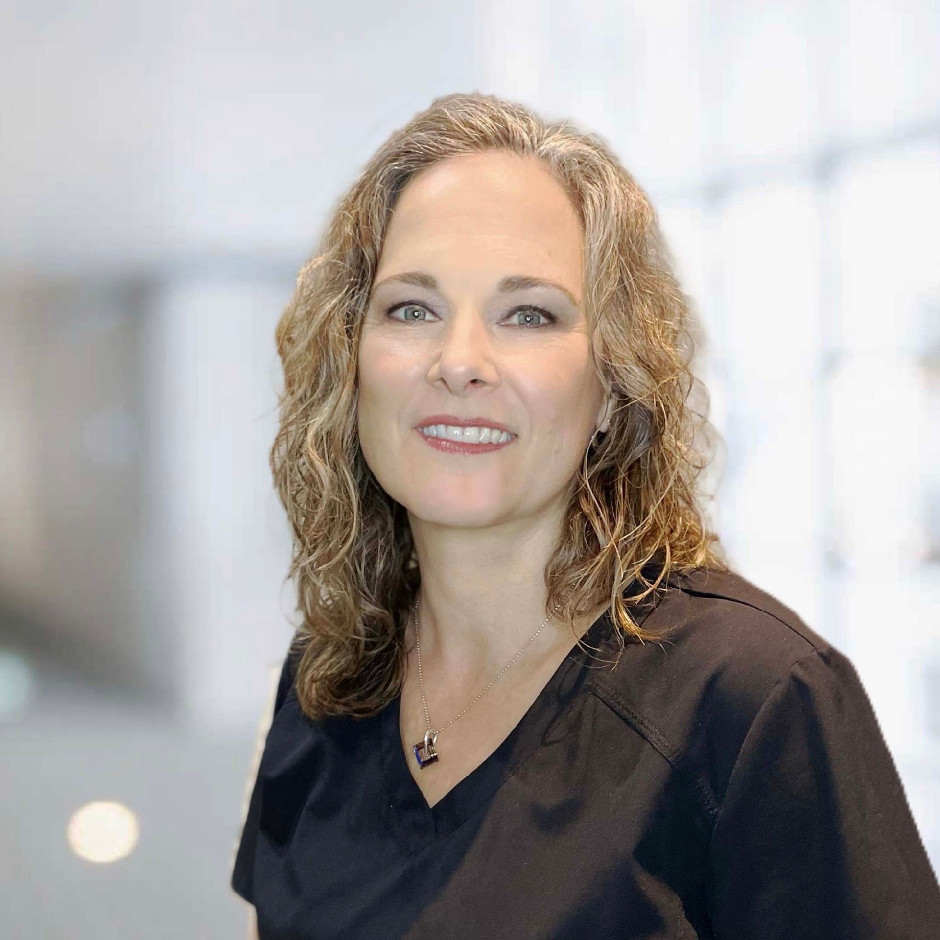 A woman in a black scrub top is smiling for the camera.