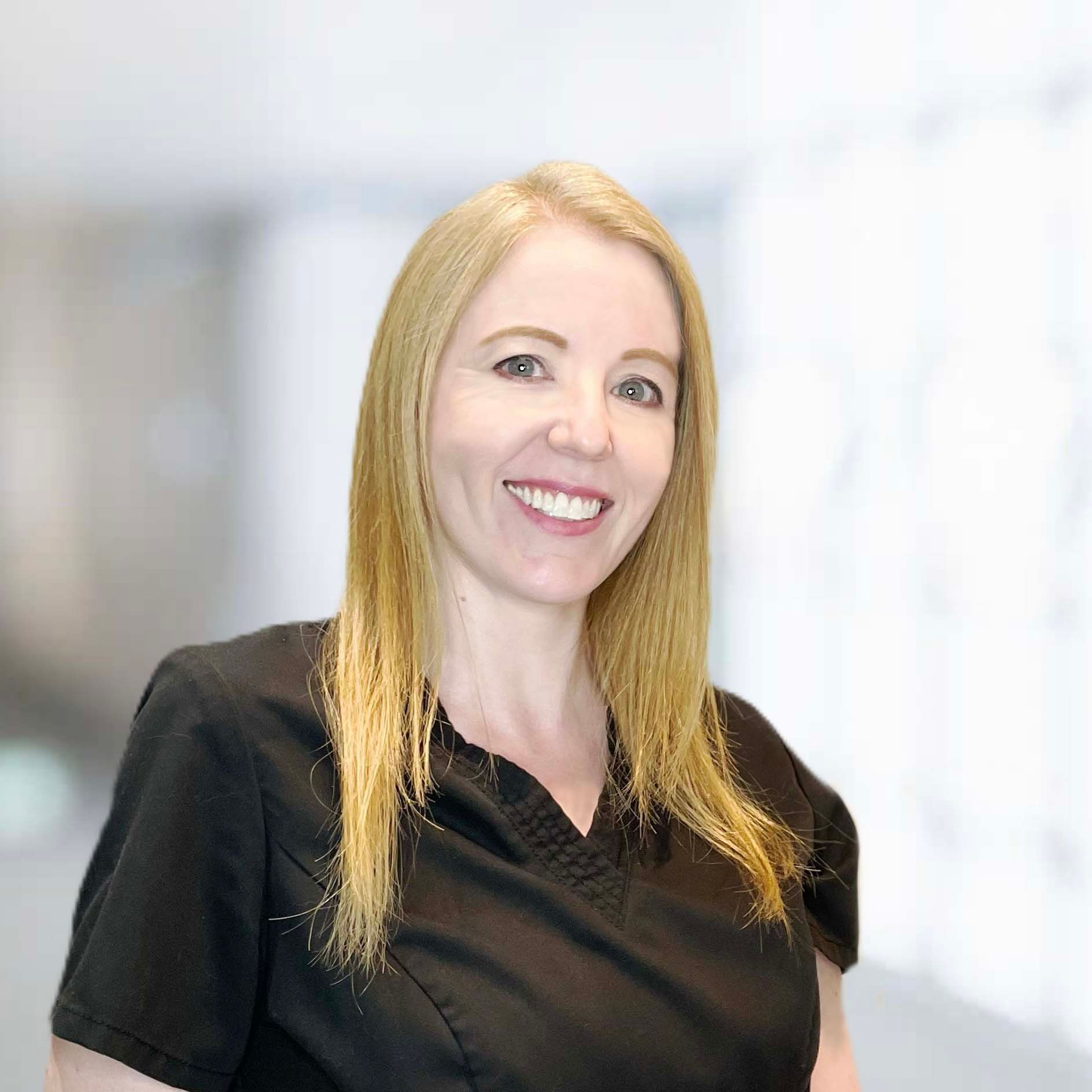 A woman in a black scrub top is smiling for the camera.