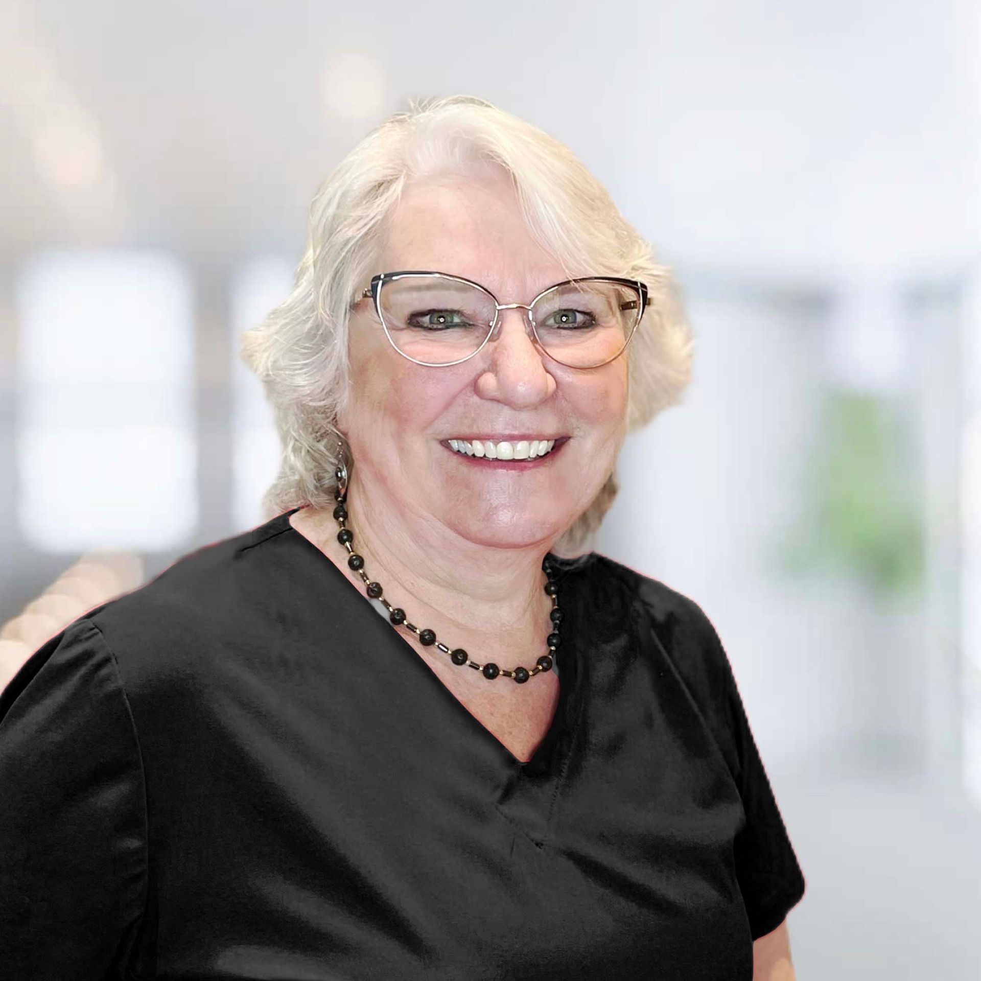 A woman wearing glasses and a necklace is smiling for the camera.