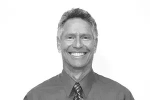 A man in a red shirt and tie is smiling in a black and white photo.