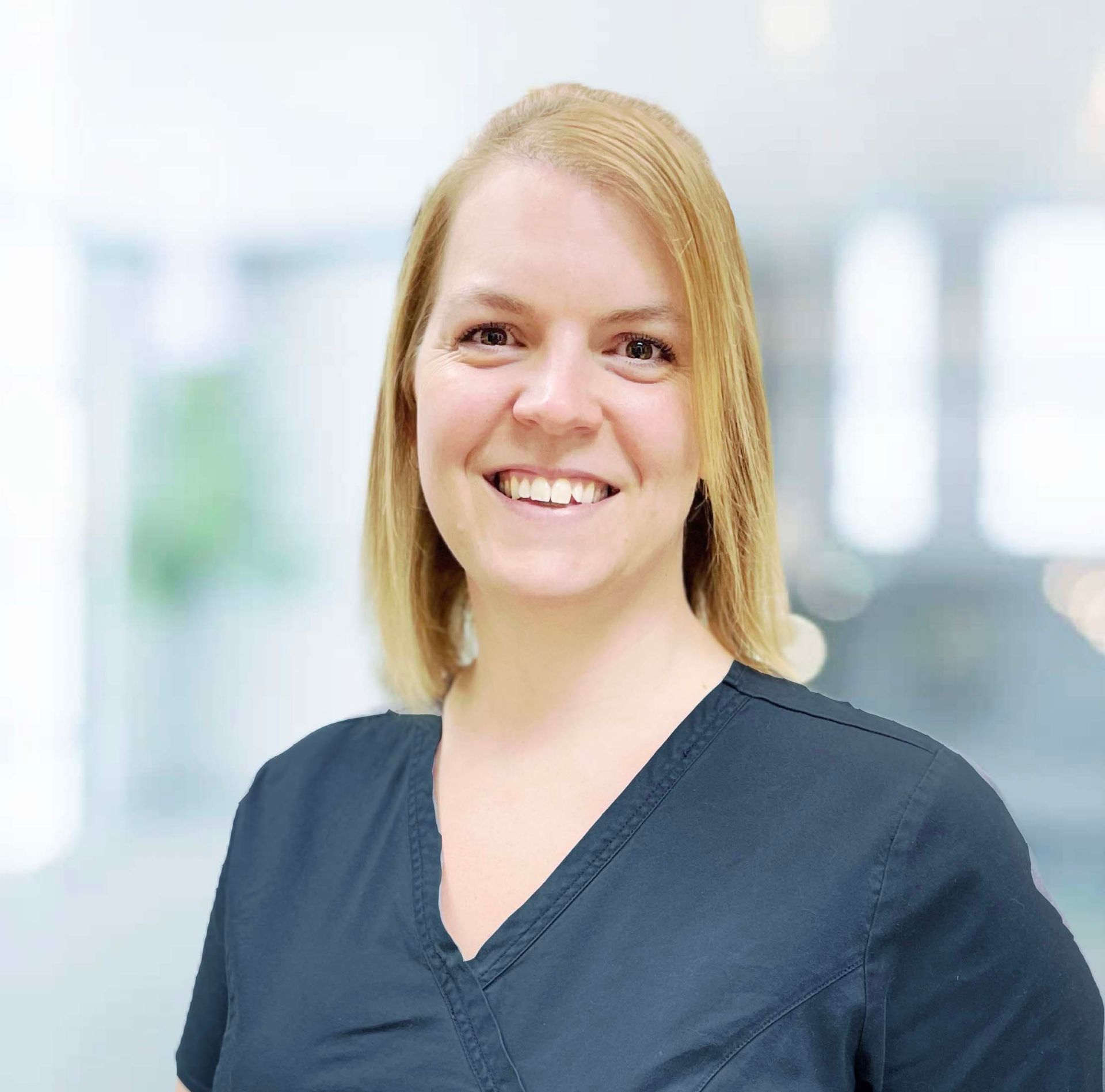A woman in a black scrub top is smiling for the camera.