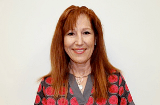 A woman with red hair is smiling and wearing a polka dot shirt.