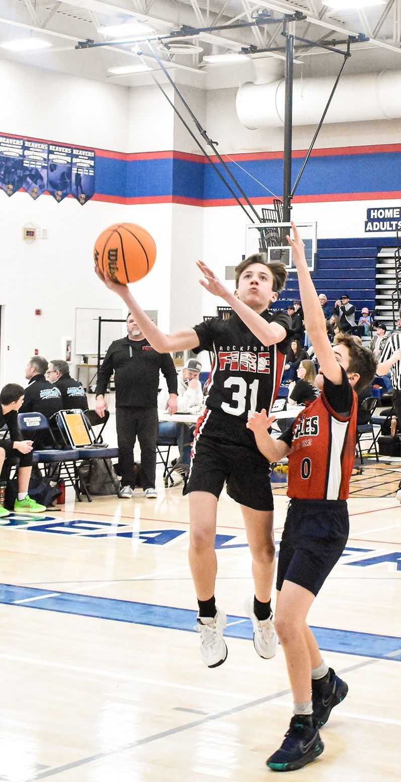 Basketball player in black jersey drives to the hoop while defender in red contests inside a gym