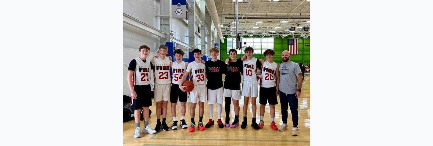 Group of basketball players posing together in a gym, wearing white and red jerseys.