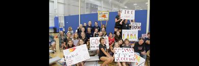 Group of people posing indoors at a community event, holding handmade signs and banners.