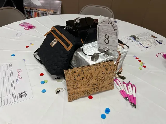 A table centerpiece for event number 8, featuring two handbags, several pens, and a sign on a white tablecloth.