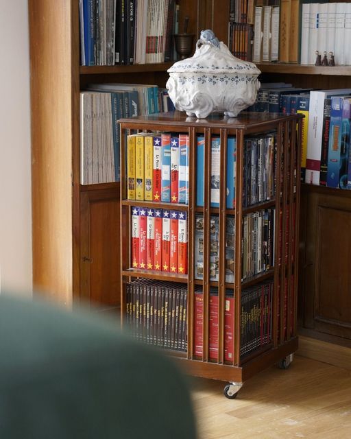 Leggio in legno con ruote, con libri colorati in una stanza accogliente, sormontato da un paralume bianco.