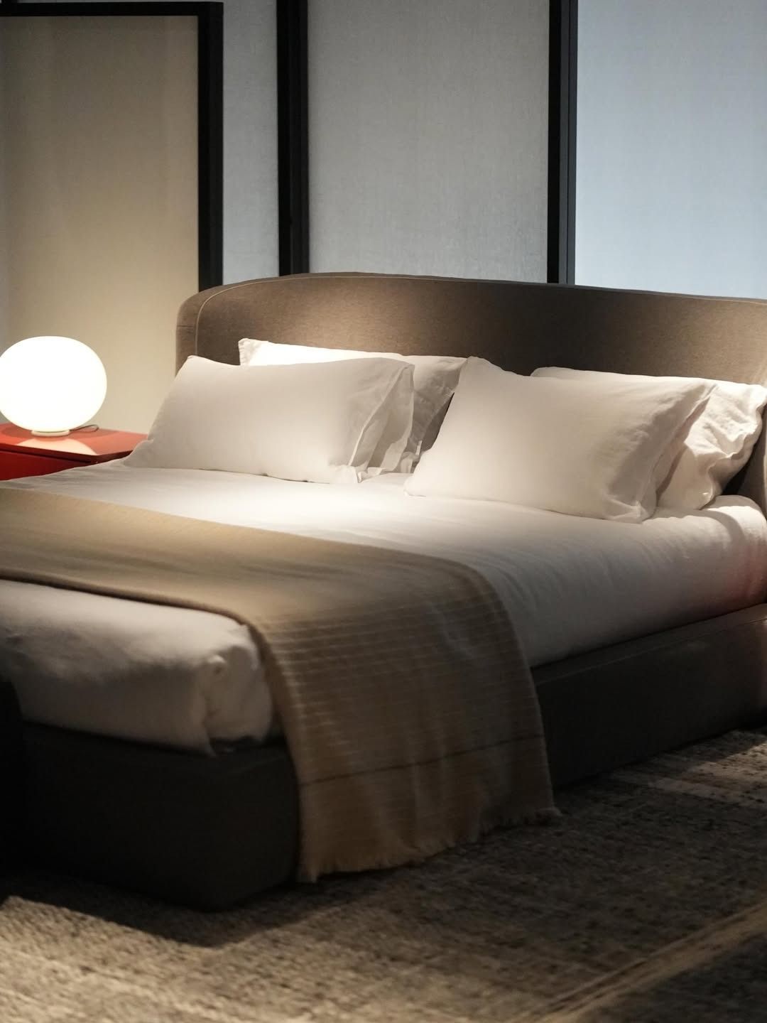 Camera da letto moderna con letto ben rifatto, cuscini bianchi e una lampada da comodino luminosa.