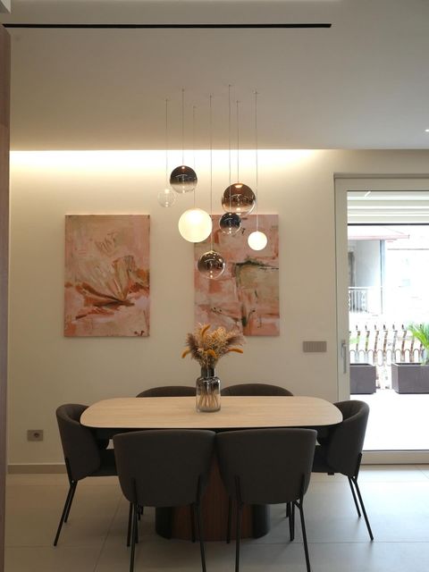 Sala da pranzo moderna con tavolo rotondo, sedie nere, lampade a sospensione e opere d'arte alle pareti.
