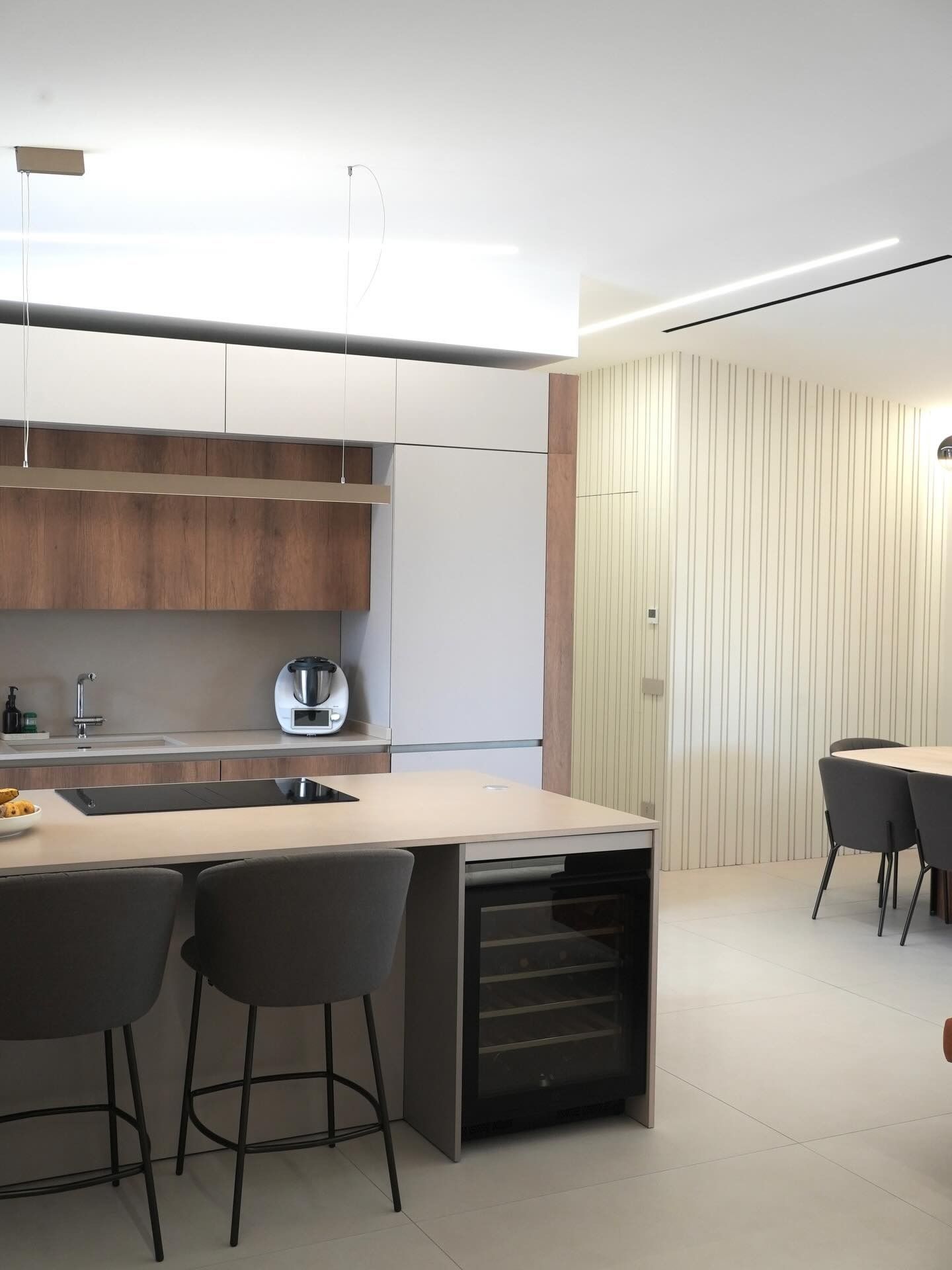 Cucina moderna con isola, sgabelli da bar, mobili in legno e zona pranzo in un luminoso ambiente open space.