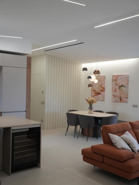 Soggiorno moderno a pianta aperta con divano marrone, tavolo da pranzo, quadro astratto alla parete e decorazioni dai toni neutri e delicati.