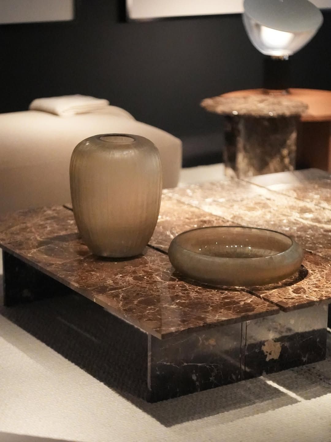 Vasi di vetro su un piedistallo di marmo marrone, esposti in una galleria scarsamente illuminata.